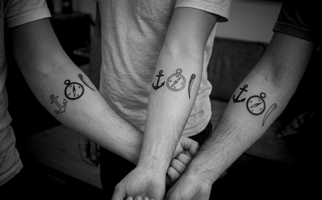 Three friends showing tattoos on their forearms &mdash; anchor, compass, and marlinspike